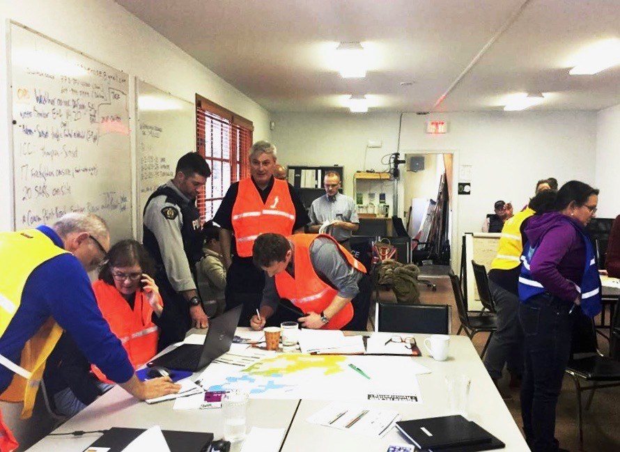 Municipal hall with a dozen people, many wearing high-vis vests and looking at papers or computers