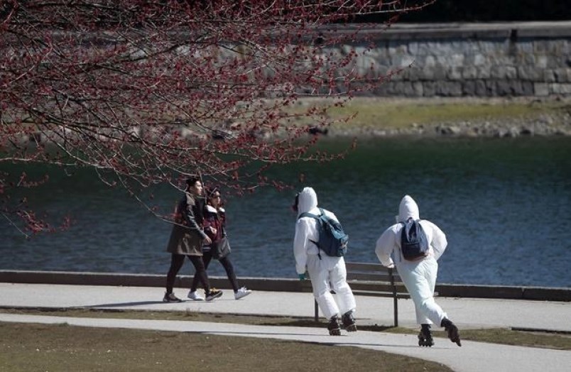 Two people wearing personal protective equipment, including respirators and coverall suits in-line skate on the seawall at Stanley Park in Vancouver on Sunday, April 5, 2020.
