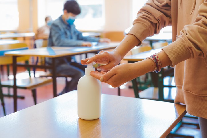 School students using hand sanitizer after entering a classroom.