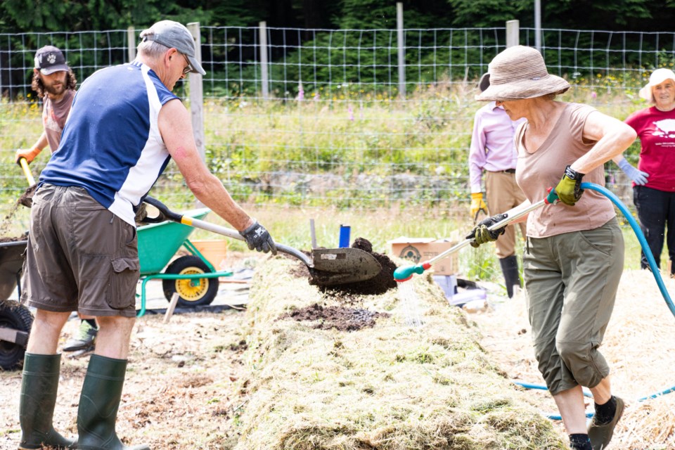 Hasan Hutchinson layers manure onto the growing lasagna bed as Susan Swift waters.