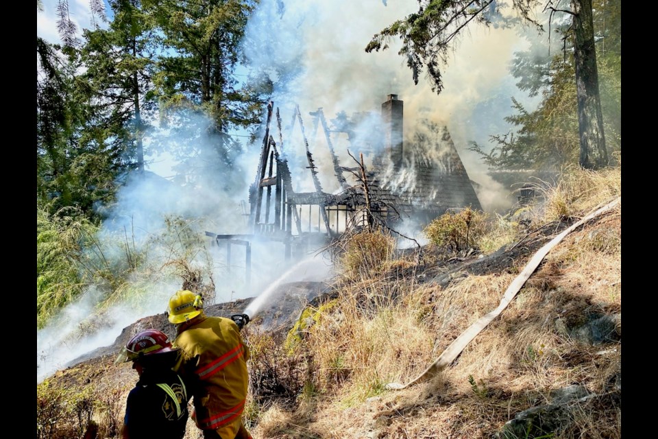 Bowen Island firefighters douse a fire in the seven hills area of Miller Rd. Wednesday. Though the home was lost, none of the surrounding buildings or homes caught fire