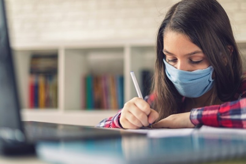 A teenager wears a mask while studying at school.