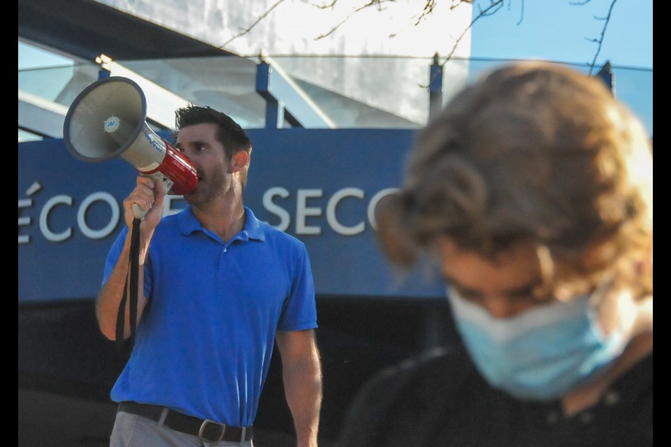 Vice-principal Joel Nelson gives instructions over a loudspeaker on new physical distancing protocols to stem the transmission of COVID-19 outside Dr. Charles Best secondary on the first day of school, Sept. 10.