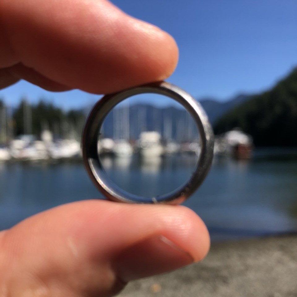 Fingers holding a ring with the boats of USSC Marina in the background