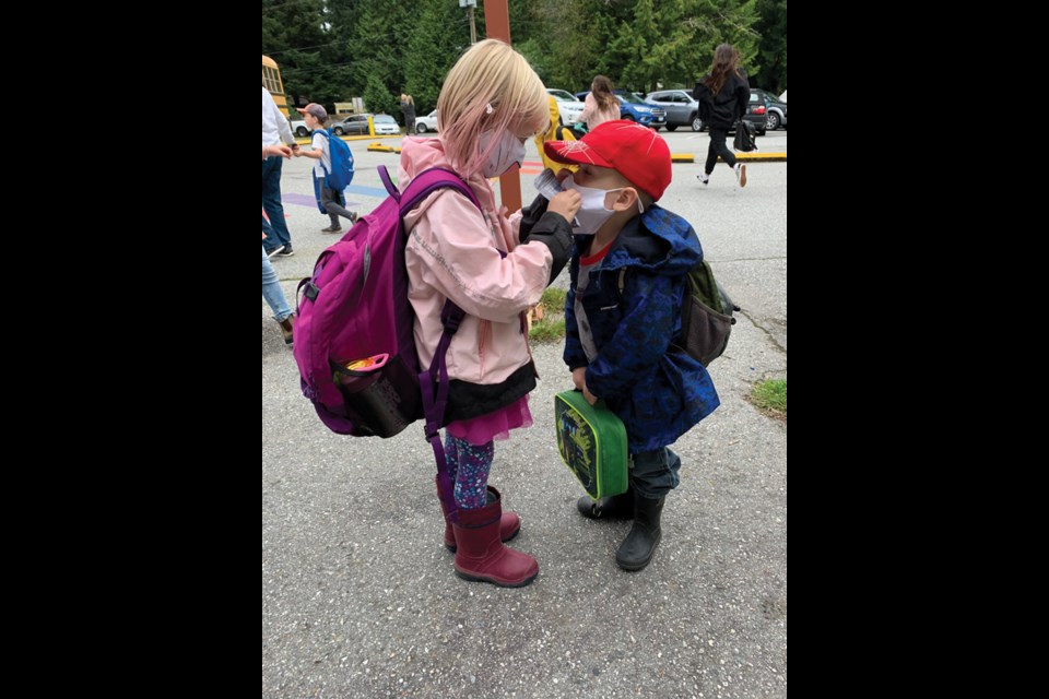 A big sister helps her brother adjust his mask at Halfmoon Bay Elementary.