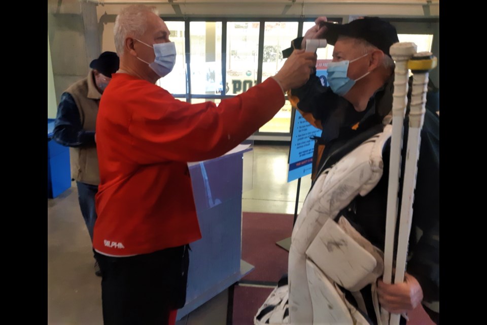 Rusty Nuts oldtimer hockey team goalie Ray Masson, 69, gets his temperature checked by defenceman Richard Larmand, 71, before their game at the Kin Centre last week. The pandemic has brought on a new reality when teams return to the rink and provincial health regulations are being enforced to keep players and their families safe.
