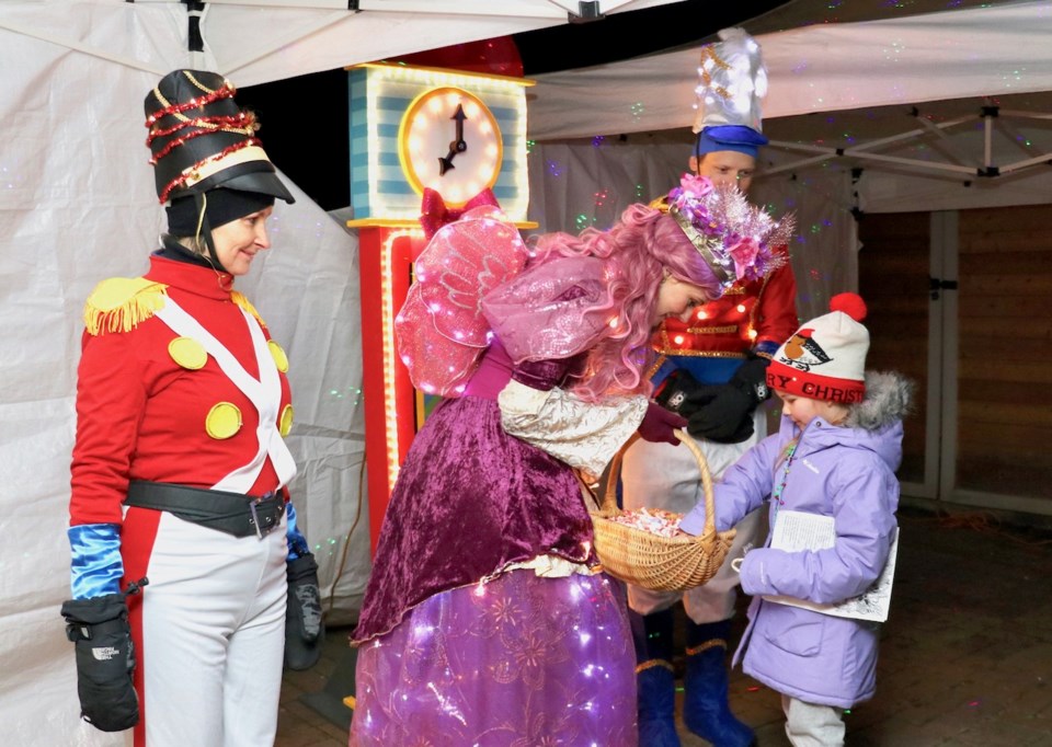 Girl picking a candy from a basket held by woman dressed as the sugar plum fairy
