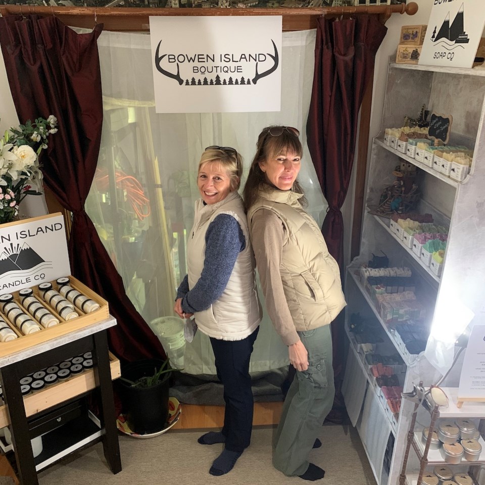 Two women standing with their backs to one another in a little shop.
