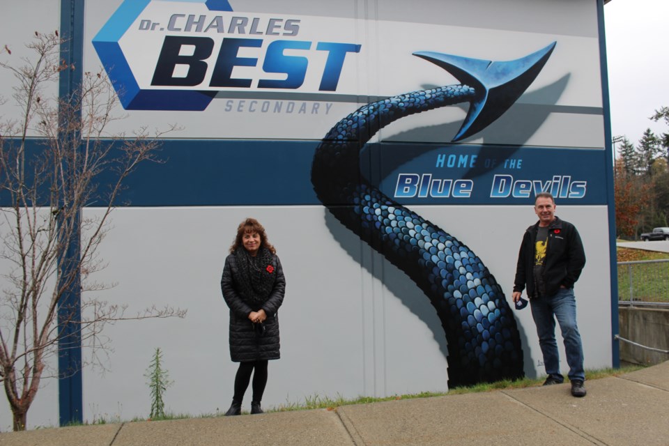 Dean Lauzé with Heather Murphy, principal at Dr. Charles Best secondary in Coquitlam, at the exterior mural the Mission resident painted under his business D’Arts.