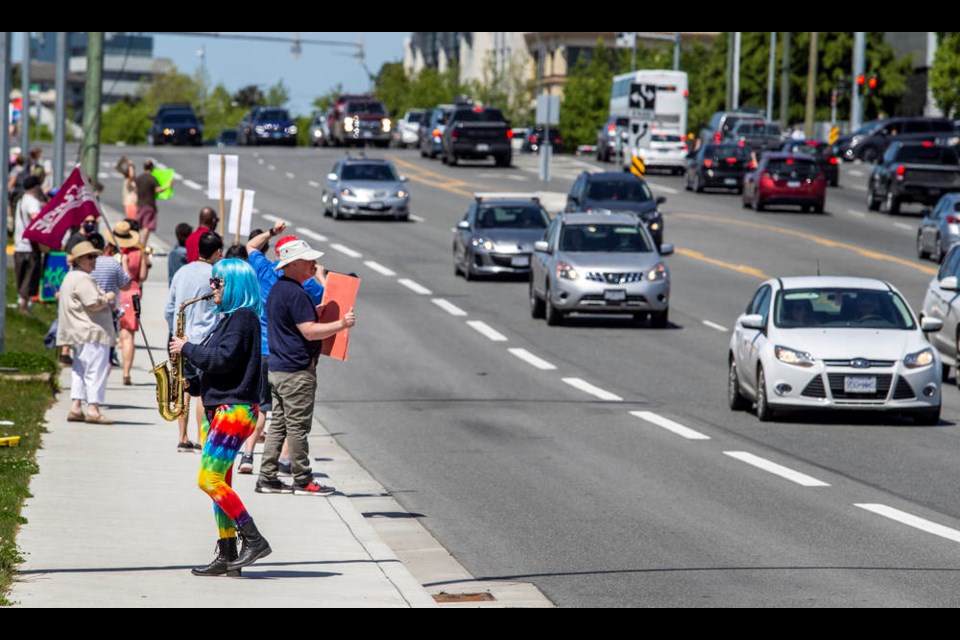 People line Douglas Street on Saturday, some of them playing musical instruments, to protest possible program cuts in the Greater Victoria school district.    [Darren Stone, Times Colonist, May 15, 2021]