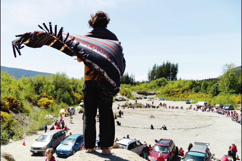 A man stands on a hill with a blanket worn like a cape, above a ceremony held by Indigenous people from the region at the Rainforest Flying Squad’s Fairy Creek HQ near Port Renfrew on May 29, 2021. NORMAN GALIMSKI