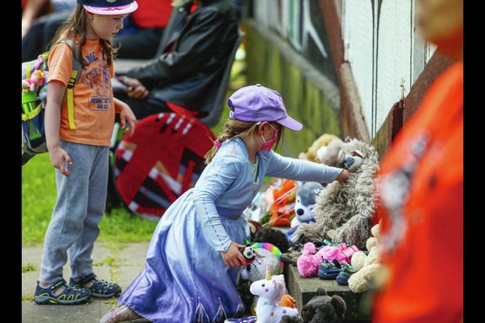 Five-year-olds Wren Danyluk, left, and Matilda Storey lay shoes and stuffed toys at a memorial outside Mungo Martins Big House at the Royal B.C. Museum on Monday. Hundreds joined in a vigil to honour the 215 children whose remains were recently found buried at the site of a former residential school at Kamloops. ADRIAN LAM, TIMES COLONIST