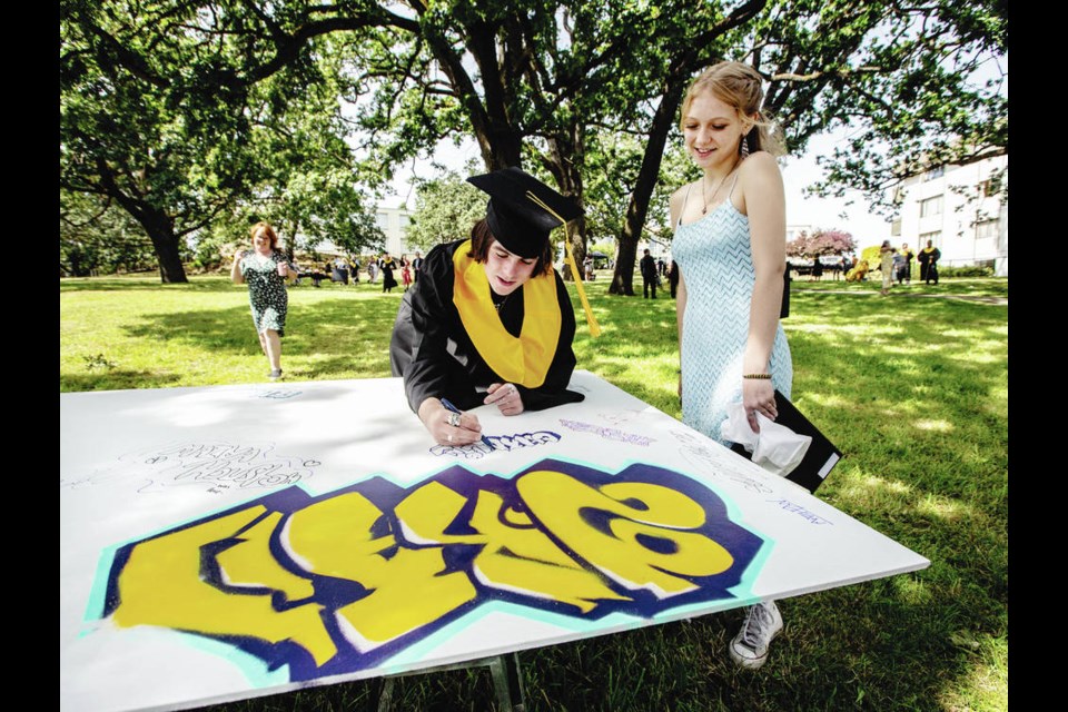 Victoria High School student Charlie Murray, 18, with girlfriend Ella Golinowski, 16, draws on a board during graduation ceremonies at the S.J. Willis campus. The board will be installed in the attic at Victoria High School when the school reopens after renovations.  PHOTOS BY DARREN STONE, TIMES COLONIST