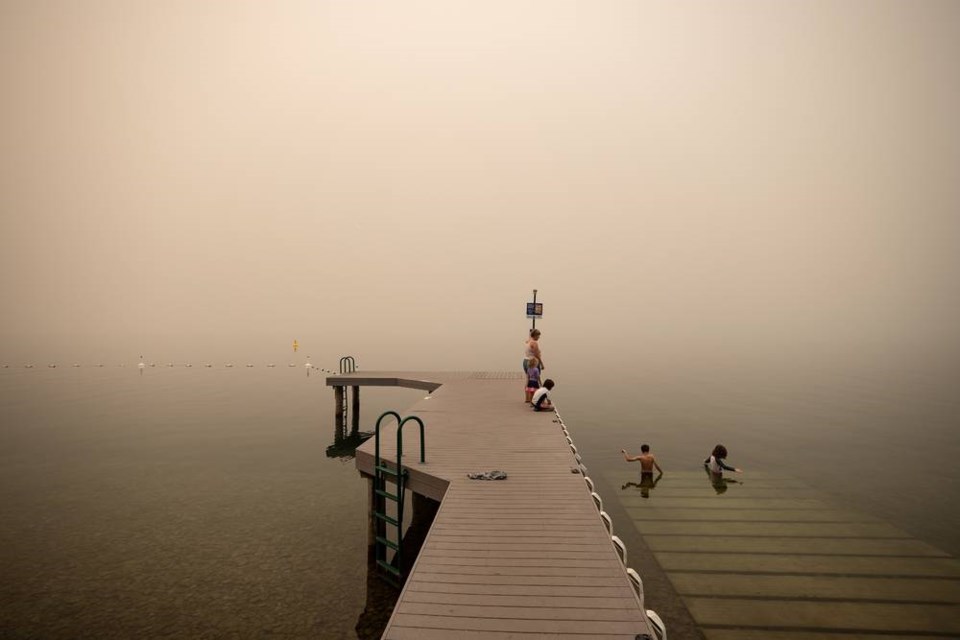Thick smoke from wildfires blankets the area as a woman stands on a pier while children look for minnows in Okanagan Lake, in Lake Country, B.C., on Friday, Aug. 13, 2021. Environment Canada has issued a heat warning and an air quality statement for much of the British Columbia coast and interior. THE CANADIAN PRESS/Darryl Dyck