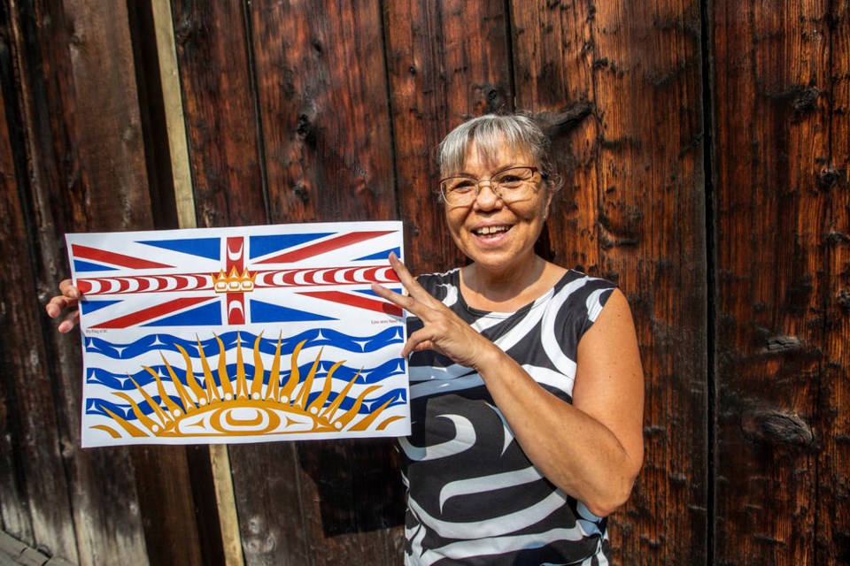Lou-ann Neel at the Royal BC Museum Thunderbird Park poses with a print of her digitally redesigned B.C. flag she made with First Nations elements. She plans do an painting of it to auction to raise funds for the Indian Residential Schools Survival Society. DARREN STONE, TIMES COLONIST