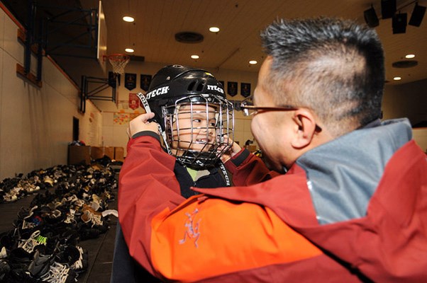 Does it fit? Mel Madrazo fits his son Micah, 5, for a hockey helmet at the KidSport New Westminster equipment sale on March 10.