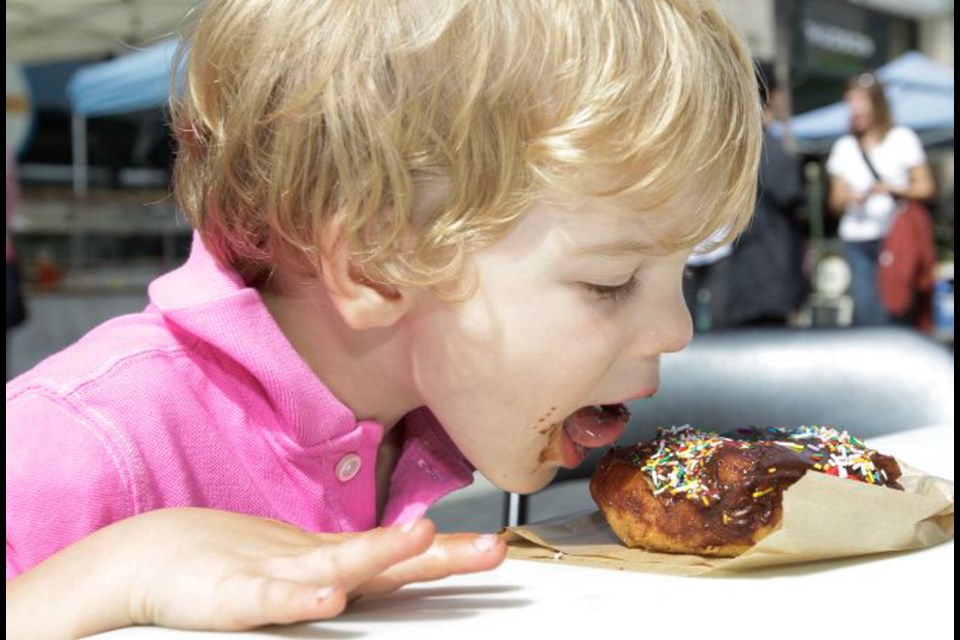 Nolan Rossato, 3, tackles a treat called a Sparkler ã a brioche with chocolate ganache and candy sprinkles ã from Doughboys Donuts at the Farmers Market at the Hudson.
