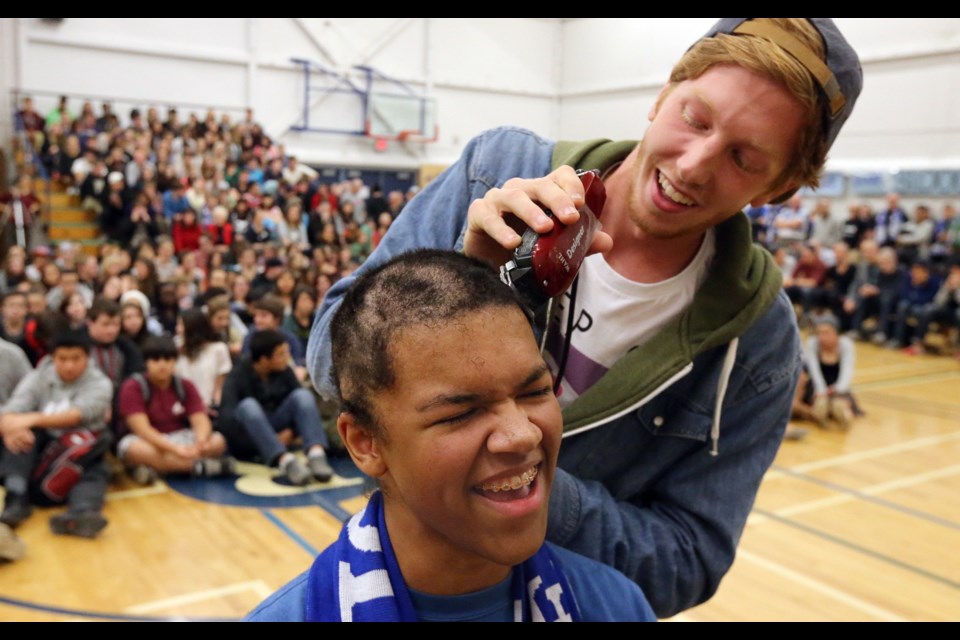 Student Wyatt Rose cuts Steven Arnold's hair prior to the Tour de Rock stop at Reynolds Secondary School on Friday.