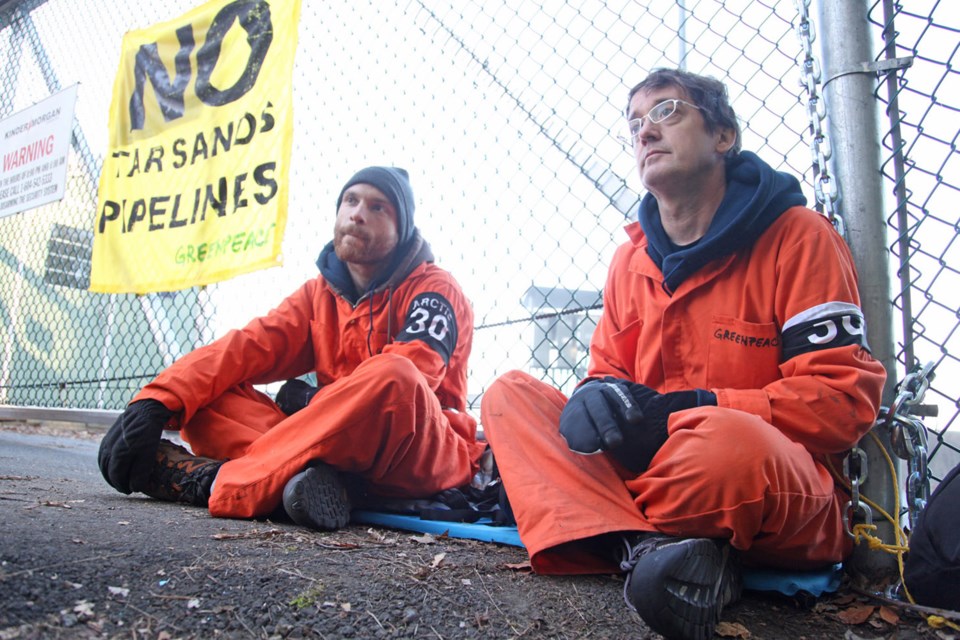 Making a statement: Greenpeace activists Benjamin Zielinski, left, and Dr. Keith Stewart chained themselves to the fence at Kinder Morgan’s Westridge Marine Terminal. At right, a protester lends his support to their cause.