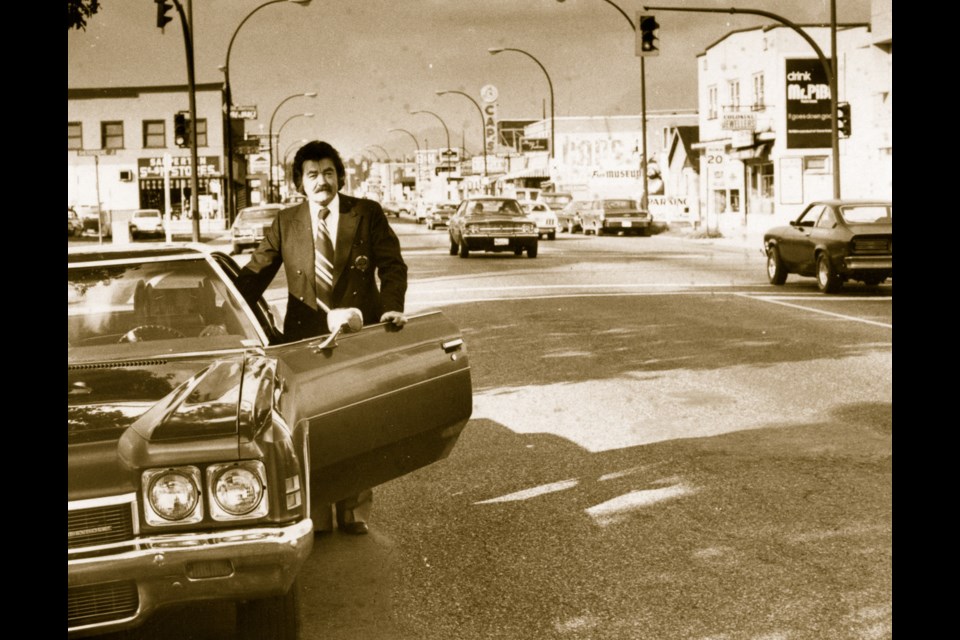 A photo of William (Bill) Anderson with his car on East Columbia Street circa 1977. Cap's Bicycle Shop is seen in the background with other businesses.