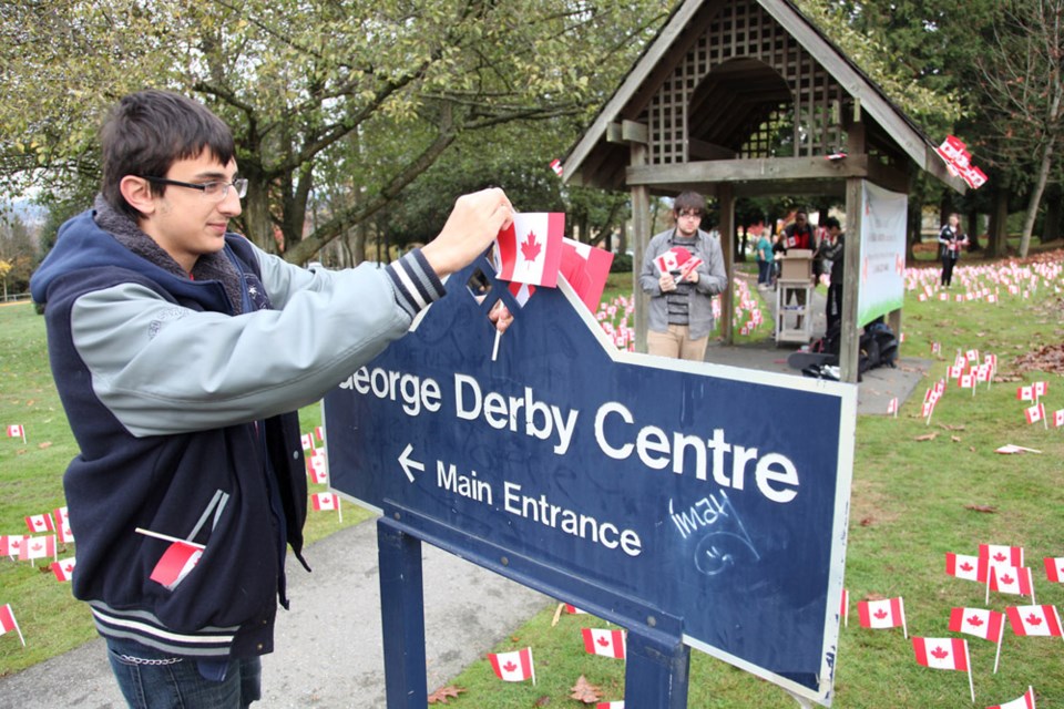 Cariboo Hill student Curtis Parent places a Canadian flag on the sign at the George Derby Centre for Remembrance Day.