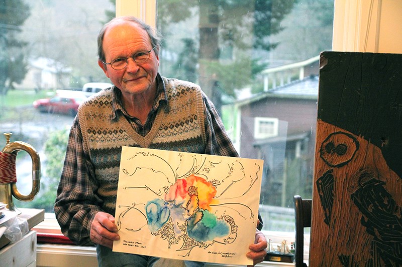 Hans-Christian Behm holds a piece of his calligraphic watercolours and stands behind a wood block carved for printing. Since Capilano University shut down its Art Institute, Behm has been working from his tiny Snug Cove apartment.