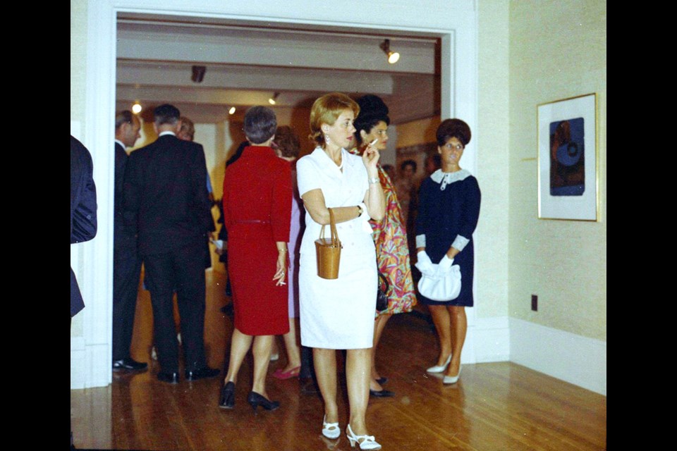 Then: Then photo: Patrons mingle at an exhibition opening at the gallery in 1966. In the foreground, a woman in a white dress smokes a cigarette as she studies the blue painting hanging on the wall.