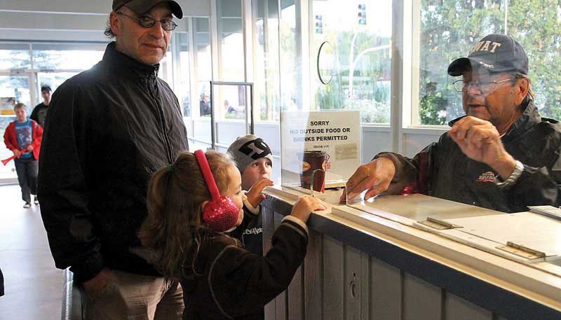 Rod Mertin stands by as his daughter Molly, 5, and son Cory, 7, purchase their tickets from volunteer Paul McKay at Saturday's Spruce King game against the Penticton Vee's at the Prince George Coliseum.