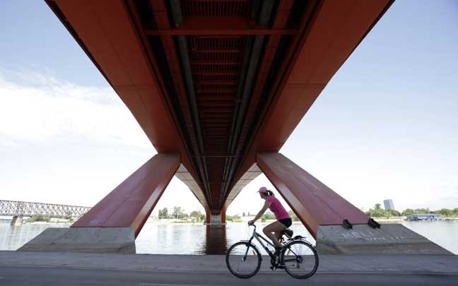 A woman cycles under the Gazela (Gazelle) bridge on the bank of Sava river in Belgrade, Serbia, Wednesday, May 22, 2013. (AP Photo/Darko Vojinovic)