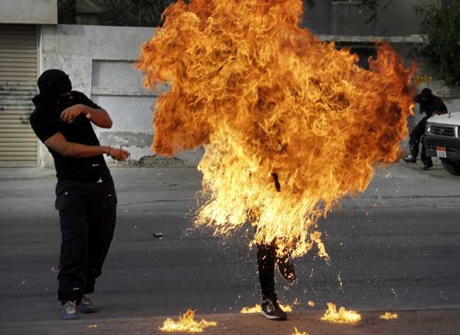 A Bahraini anti-government protester is engulfed in flames when a shot fired by riot police hit the petrol bomb in his hand that he was preparing to throw during clashes in Sanabis, Bahrain, Thursday, March 14, 2013. Protests and clashes erupted in opposition areas nationwide Thursday with government opponents observing a "Dignity Strike" blocking roads, closing shops, protesting and staying home from work and school called by the more radical February 14 youth group. (AP Photo/Hasan Jamali)
