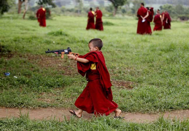 A novice Tibetan Buddhist monk plays with a toy gun during a break from their spiritual leader the Dalai Lama's religious sermon outside the Gyudmed Tantric Monastery in Gurupura 212 kilometers (132 miles) southwest of Bangalore, India, Monday, July 15, 2013. The Dalai Lama is in Gurupura till July 16 for Buddhist religious teachings. (AP Photo/Aijaz Rahi)
