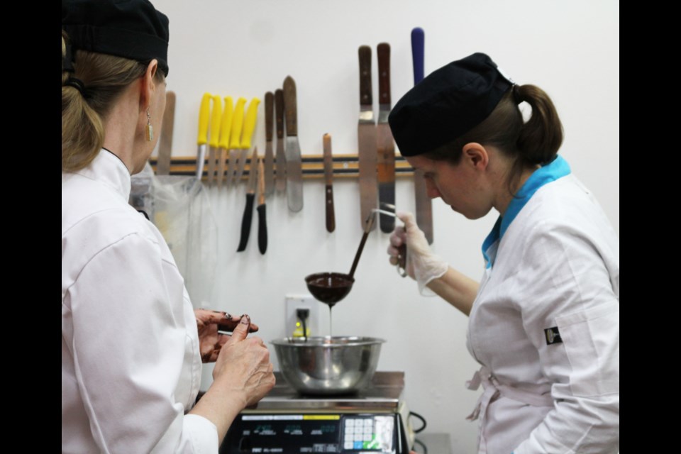 Cocoa West Chocolatier Joanne Mogridge coaches a student through the process of creating chocolates that will be formed in a mold.