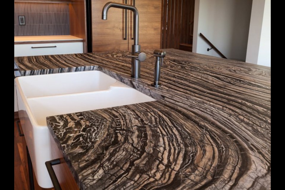 A deep, farmhouse-style, enamelled sink is set in a striking silver wave marble countertop that looks chocolate swirl ice cream.