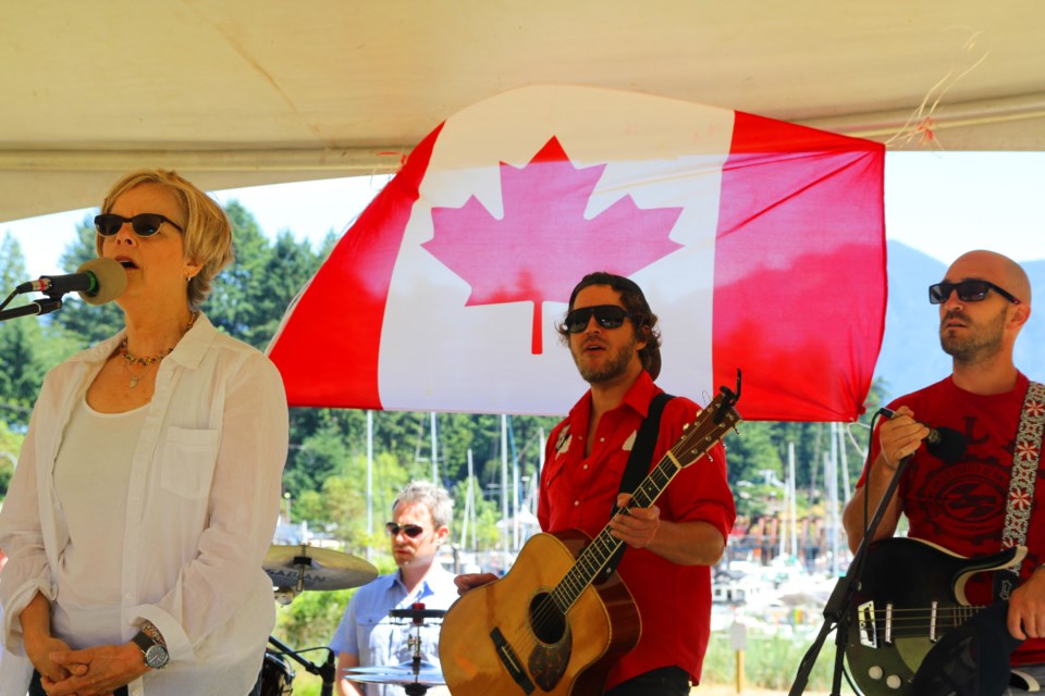 Shari Ulrich sings O Canada to kick of this year’s Canada Day celebrations at Crippen Park. Drummer Jesse Godin, Adam Woodall and Todd Taylor stand behind her. Not visible, other Adam Woodall Band member: bass player Dave Hall.