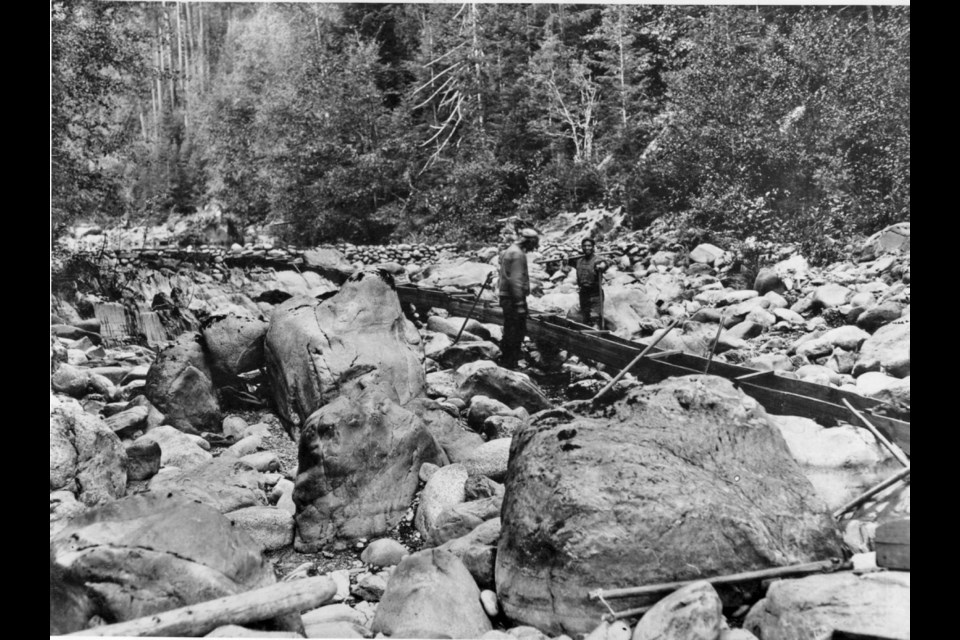Chinese miners standing beside a flume in a riverbed near Leechtown. Image D-07529 courtesy of Royal BC Museum