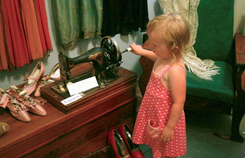 A young girl plays with an old sewing machine from England, while trying to complete her world traveler&#8217;s passport.