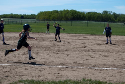 A Carlyle under 12-years-old player runs hard for first base beating the play as the Oxbow shortstop attempts to get her out.