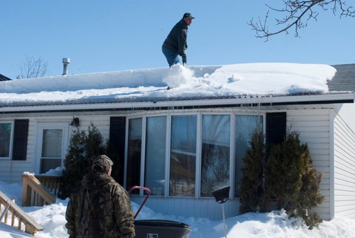 Residents shovel snow, over a foot deep, off of their roof.