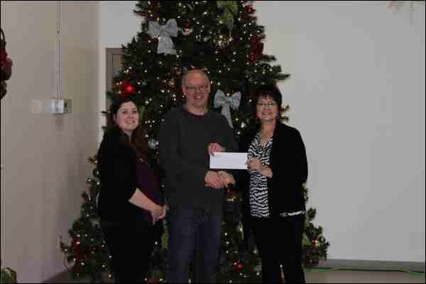 Jolene Renas, WDM administrative assistant (right), Shirley Hujber, WDM customer service assistant (left) present Bill Hall of the Battlefords Empty Stocking Fund with a cash donation raised by the Western Development Museum North Battleford at a  staff function auction in December.