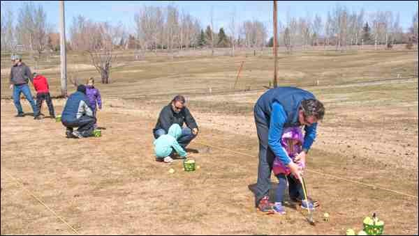 Parents help their kids hold their club at the driving range.
