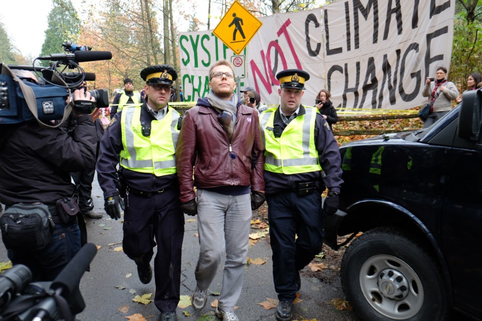 Police lead a protester away from Burnaby Mountain on Centennial Way, where RCMP have started making arrests so Kinder Morgan crews can finish survey work for a new pipeline route.