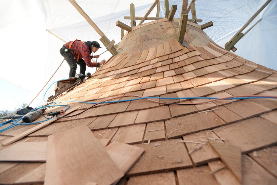 A worker puts the finishing touches on the cedar shingle roof covering the new aboriginal carving pavilion behind Britannia secondary school.