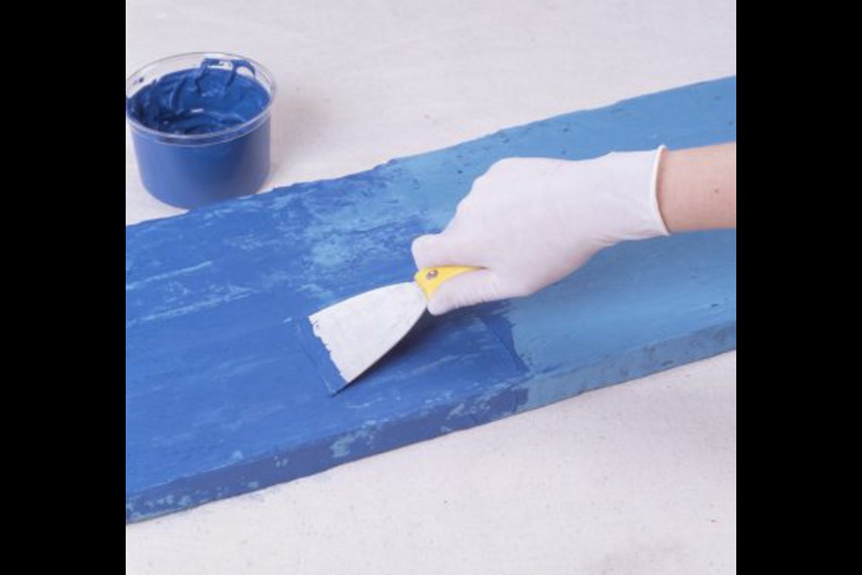 A thin coat of dark blue plaster is smoothed over the board with a spatula, allowing some of the light blue plaster to show through.