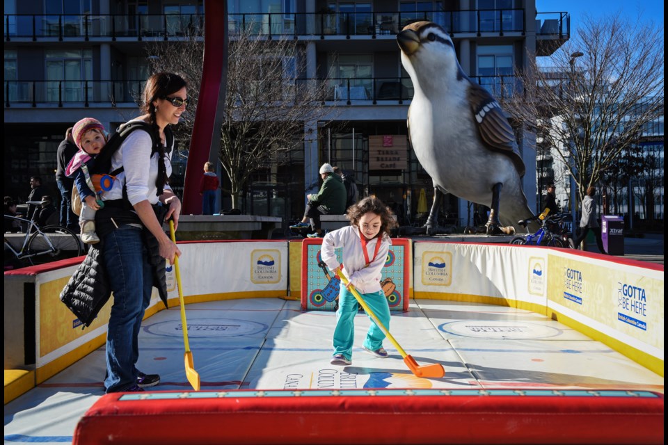 Moonwater plays a little hockey with daughter Tayen Withrow, 4, while Nyla Withrow, 1, has a comfortable seat. The family drove from Washington State for the sole purpose of attending Sunday’s Winter Games Legacy Celebration at the Southeast False Creek Olympic Plaza. Photograph by: Rebecca Blissett