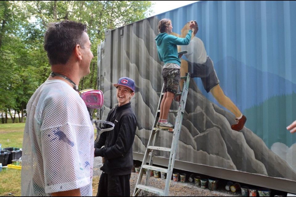 Artist Todd Polich, left, shares a laugh with Take a Hike student Gabe Lance, middle, and fellow artist Emily Gray during the painting of a storage container recently donated to the Take a Hike program.