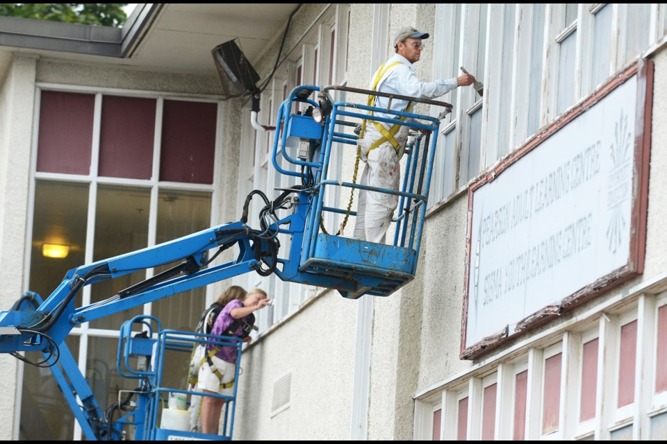 Workers paint window frames at New Westminster Secondary School.