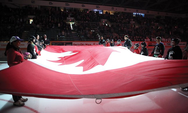 Players and parents from the Prince George Cougars Hockey School wave a large Canadian flag during the National Anthem on Friday at the CN Centre as the Prince George Cougars played their home opener against the Everett Silvertips.