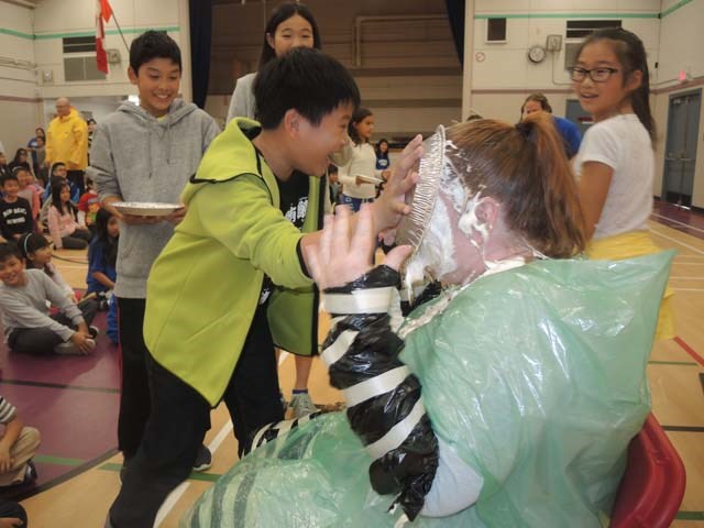 Students line up with pies full of cream and marshmallows for their teacher at Errington elementary