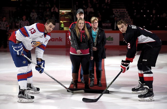As parents Craig Tott, and Michelle Tott look on, Delany Tott, sister of Pte Kirby Tott, drops the puck in a ceremonial faceoff as the Prince George Cougars celebrated Heros Night on Friday during their game against the Edmonton Oil Kings.