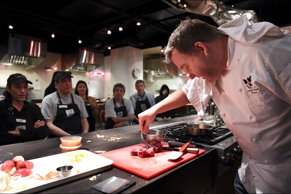 Chef David Robertson, owner and chef at the Dirty Apron cooking school, demonstrates how to prepare ingredients before sending students to their own stations to make the meal themselves. Photo Dan Toulgoet